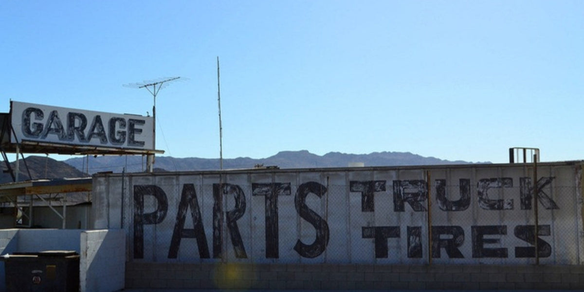 Hand-painted GARAGE and PARTS TRUCK TIRES signs under a clear desert sky